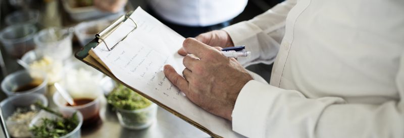 A person writing on a clipboard while inspecting a food process.