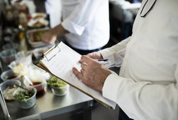 A person writing on a clipboard while inspecting a food process.